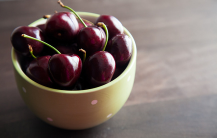 Cherries in a green bowl on a wooden worktop.