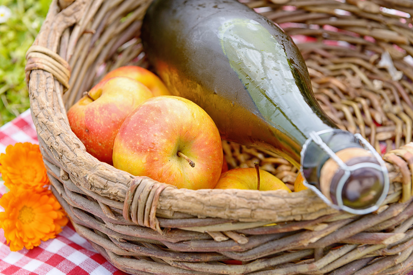 a bottle of cider with apples in a basket