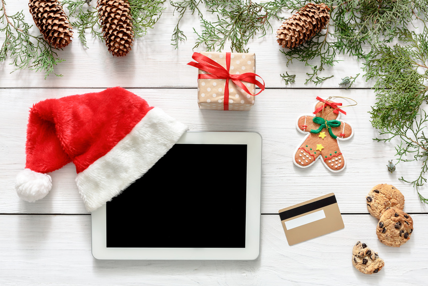 Christmas online shopping background. Tablet screen with copy space top view on white wood, credit card, present boxes and santa hat. Electronic devices, internet commerce on winter holidays concept