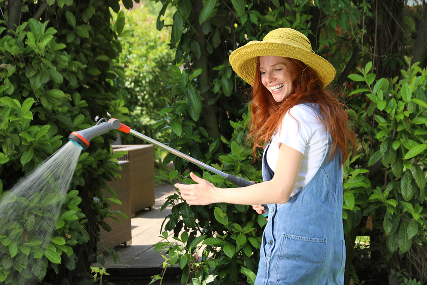 Hübsche rothaarige Frau wässert lachend mit einer Handbrause ihren Garten