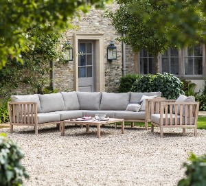 A corner sofa, table and chairs on a gravel courtyard outside a Cotswold stone house.