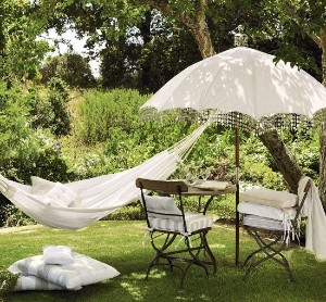 A white linen hammock and parasol beautifully framed by plants and trees.