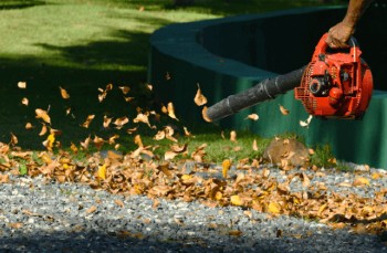 Leaves being shepherded into a pile with a handheld petrol blower.
